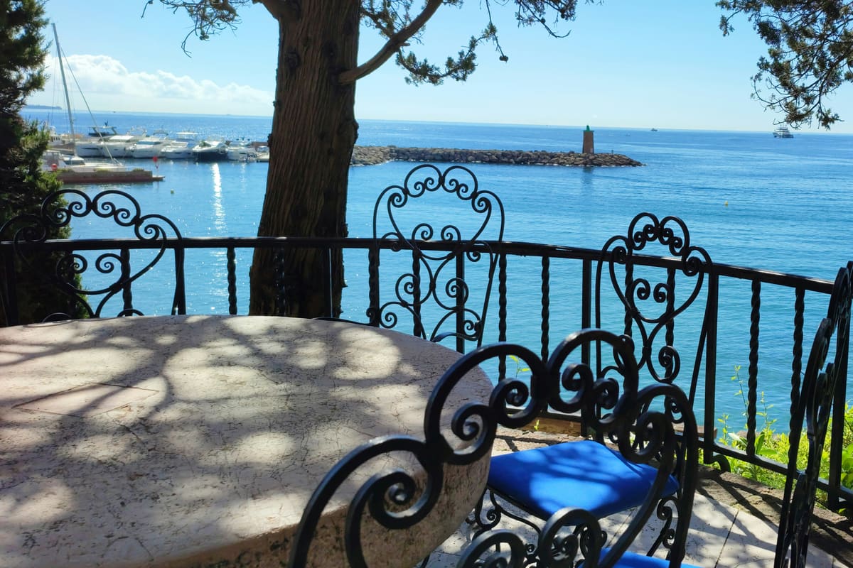 A shaded balcony table and wrought-iron chairs overlooking the sea and a small harbour