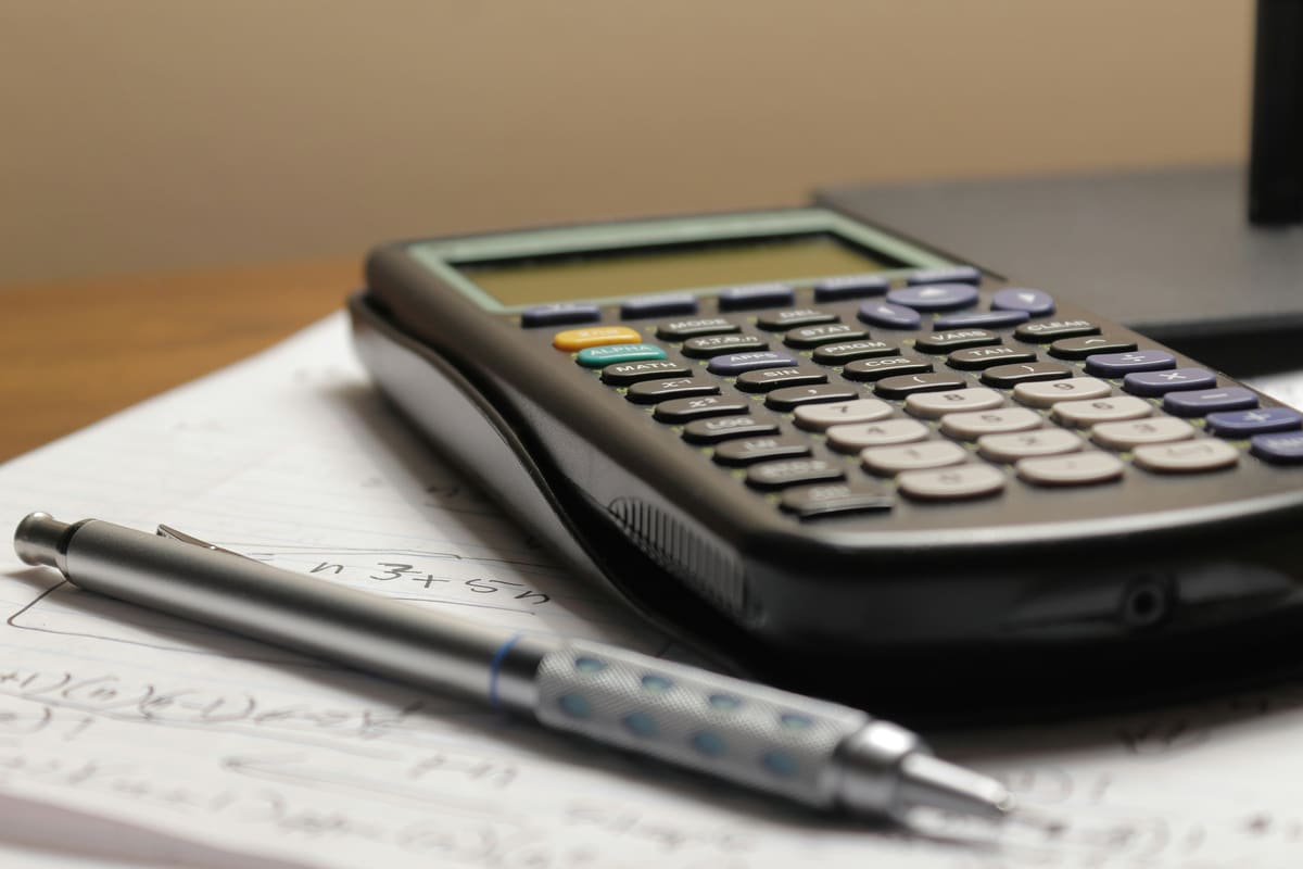 A calculator and a pen on a sheet of handwritten figures
