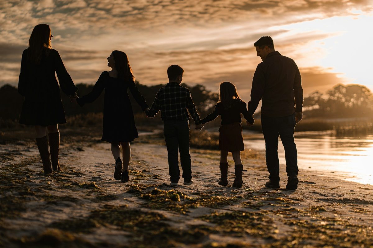 Eine fünfköpfige Familie geht Hand in Hand bei Sonnenuntergang am Strand entlang, als Silhouette