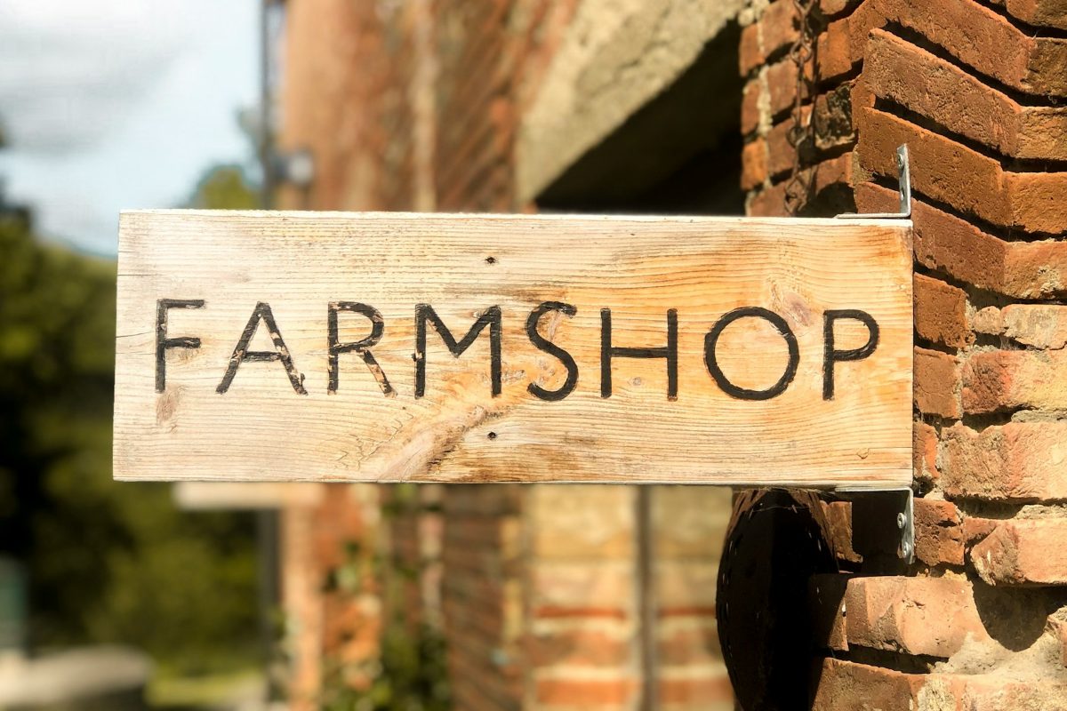 A wooden shop sign reading “Farmshop” on a brick wall