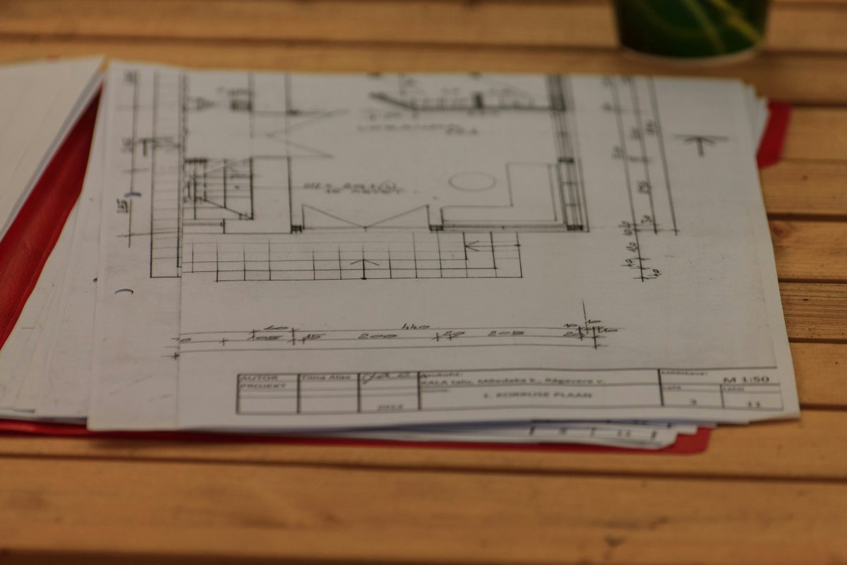 Planos arquitectónicos impresos apilados sobre una mesa de madera