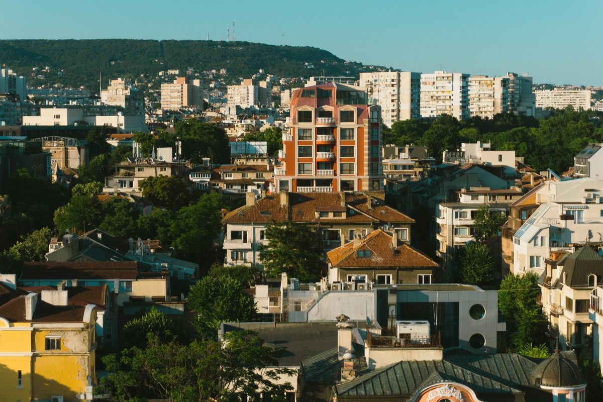 Bloques de viviendas y casas con tejados de teja entre árboles en Varna, con una colina boscosa al fondo