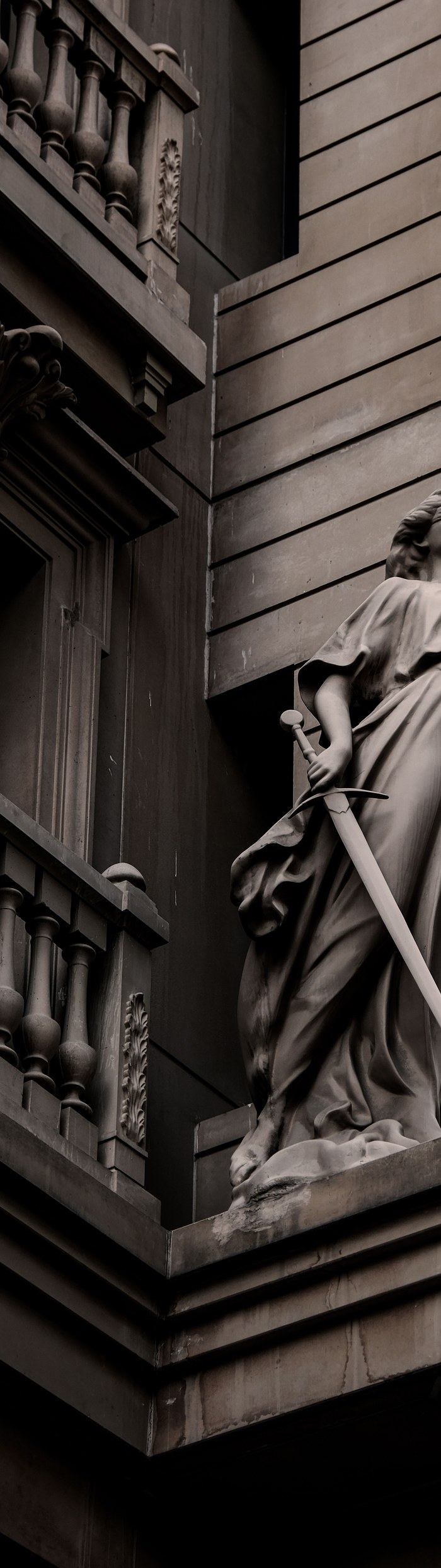 Stone statue of Lady Justice holding a sword on a historic façade